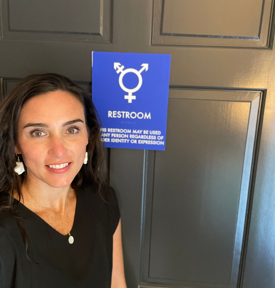 Jocie Sweeney beside an inclusive restroom sign